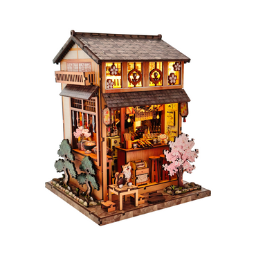 Wooden model of a traditional Japanese house with cherry blossom trees and interior lights on a white background