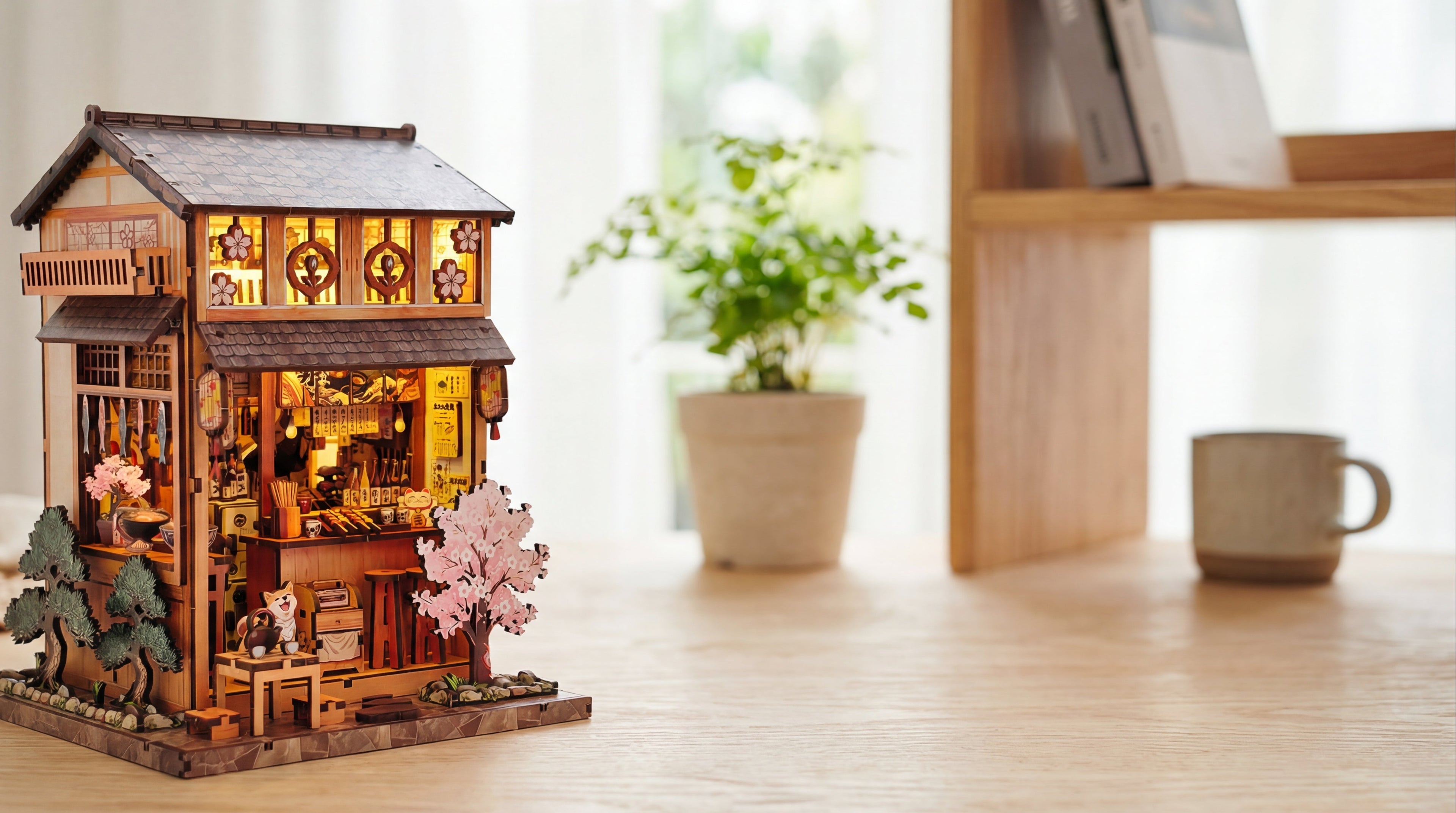 Model of a wooden house with lights on a table with a plant and mug in the background